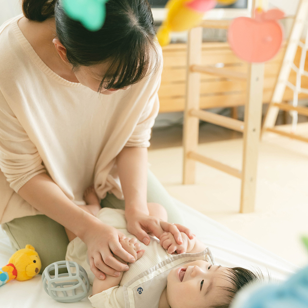 自宅のいつもの遊びスペースにてママと赤ちゃんが笑顔で触れ合っている