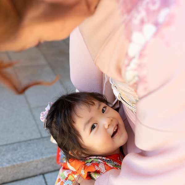 神社にて母に甘え抱きつく、赤い着物を着た幼い女の子