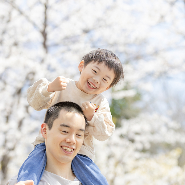 桜の花を背景に、男の子がパパに肩車をしてもらい楽しんでいる