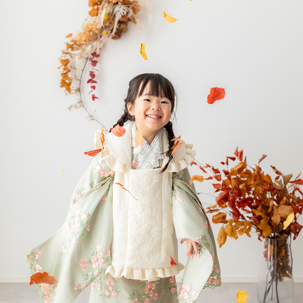 紅葉の葉っぱが散る中、鶯色の着物を着て撮影を楽しむ女の子