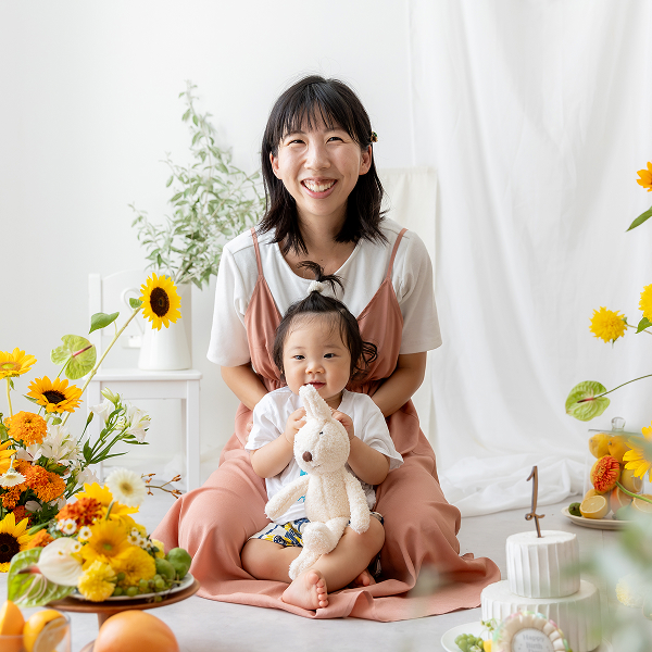 向日葵撮影会にてママのお膝にウサギのぬいぐるみを持った幼い女の子が座って揃って2人で笑顔をこちらに向けている
